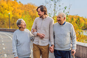 An elderly couple walks in the park with a male assistant or adult grandson. Caring for the elderly, volunteering. BANNER, LONG FORMAT