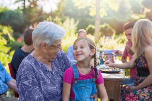 Summertime , a family of three generations having fun around a table in the garden sharing a meal. Close-up on a grandmother with her granddaughter in her lap