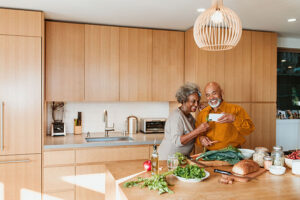 Smiling senior couple watching video while preparing vegan meal in kitchen. Retired man and woman are standing with vegetable at kitchen island. They are spending leisure time at home.